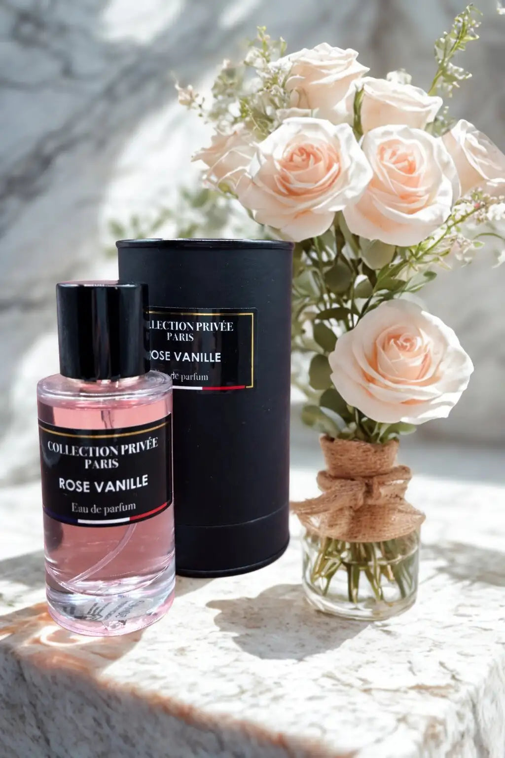 Une bouteille en verre transparent avec un bouchon noir et une étiquette, contenant un liquide rose, étiquetée ’collection privée paris rose vanille eau de parfum.’